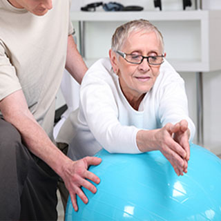 older woman being taught a physical therapy technique using a yoga ball